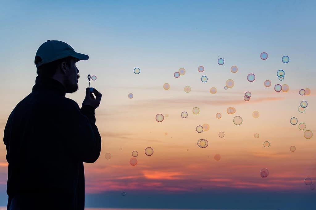 A silhouette of a man blowing bubbles at sunset, symbolizing the fleeting nature of past life memories drifting through the subconscious like echoes from another time.