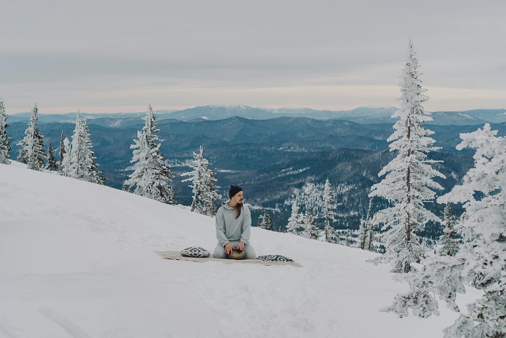A man practicing yoga at a snowy mountain.