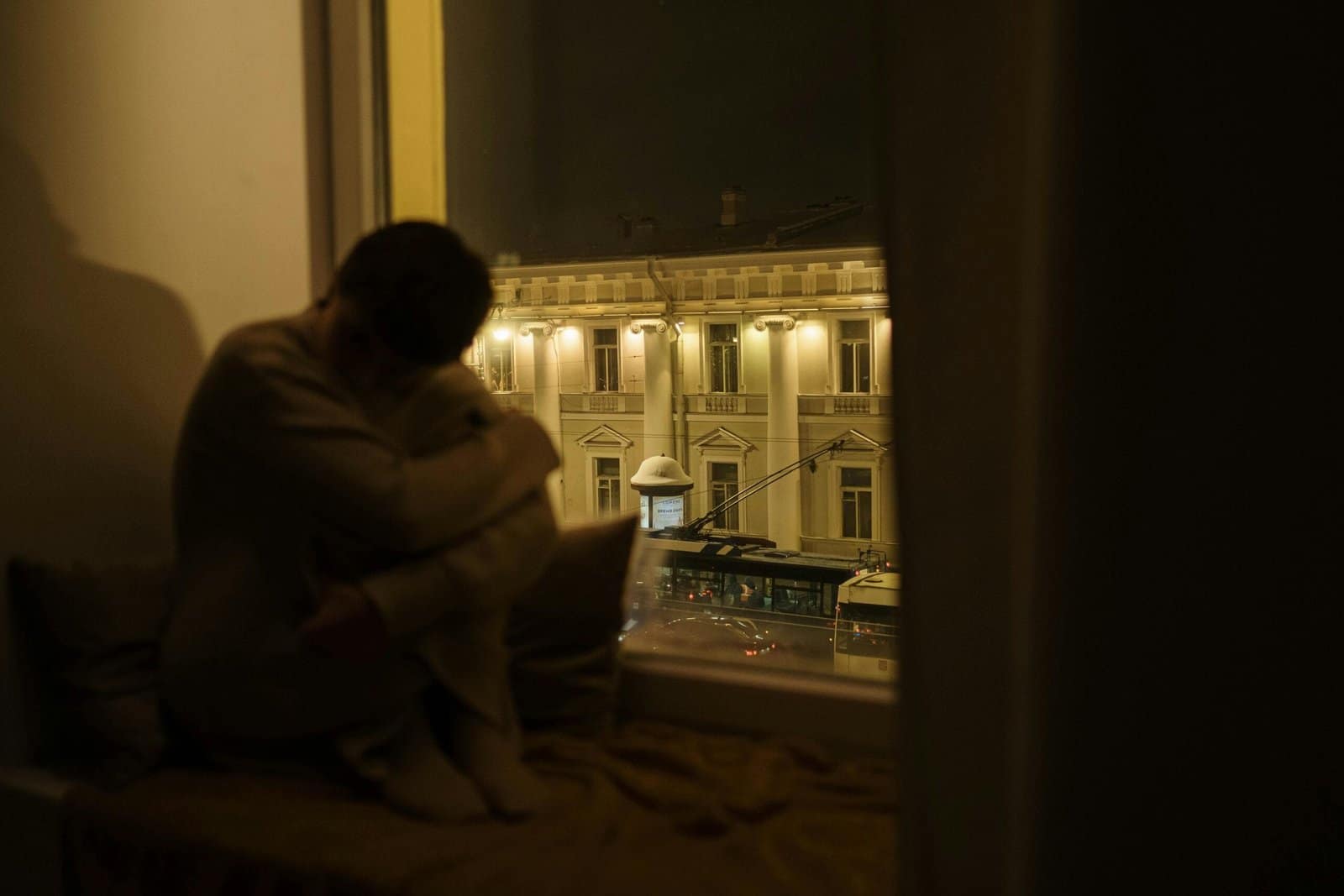 A man watching through the window trying to fight racing thoughts at night.