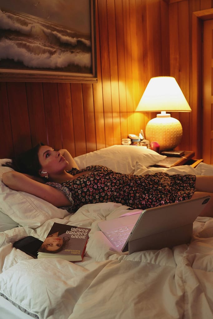 A woman lying in bed with a laptop and a book, staring at the ceiling because racing thoughts at nigth won't let her rest