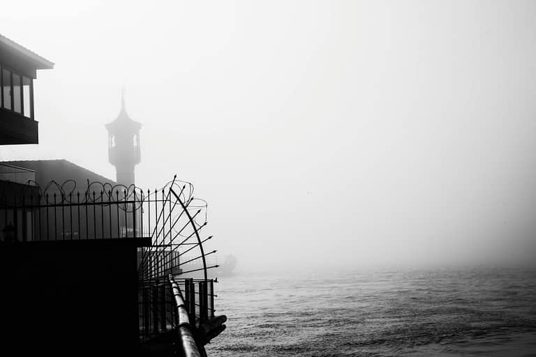 A misty waterfront with an old church tower in the distance, symbolizing introspection and spirituality, evoking thoughts on is lucid dreaming a sin.