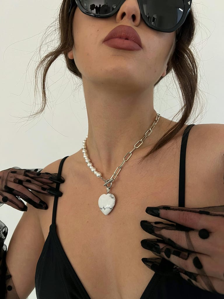 A beautiful magnetic woman's face and neck with a heartshaped necklace and black satin gloves